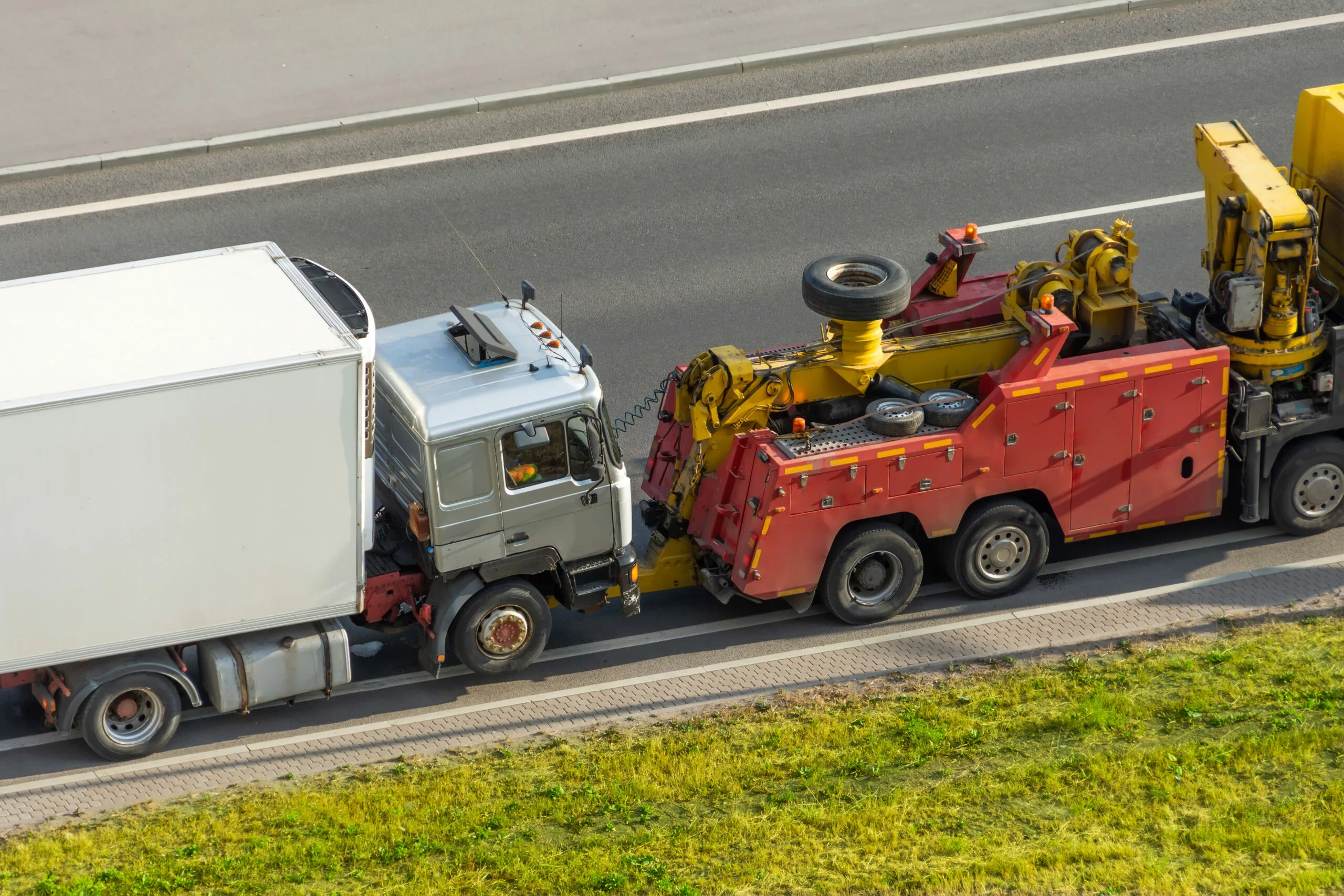 Powerful heavy duty big rig mobile tow semi truck with emergency lights and towing equipment prepare to tow broken white semi tractor standing out of service on the highway side.